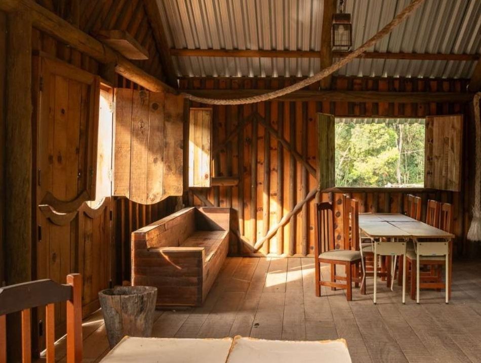 Interior do Rancho do Peão com mesas, bancos de madeira e janela para a mata